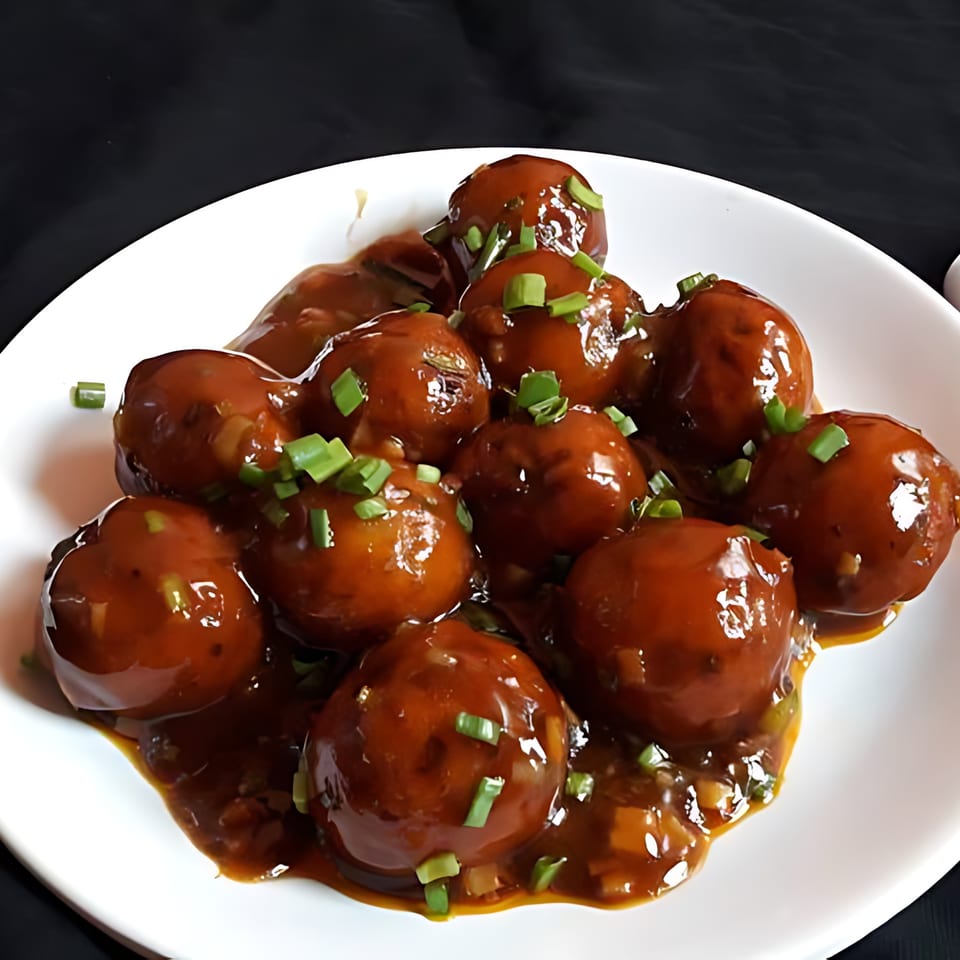 Milagu Indian Cuisine's Manchurian dish, featuring brown glazed vegetable balls garnished with green onions on a white plate.
