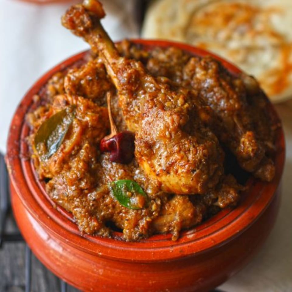 Milagu Indian Cuisine's spicy chicken curry with drumsticks, garnished with chili and curry leaves.