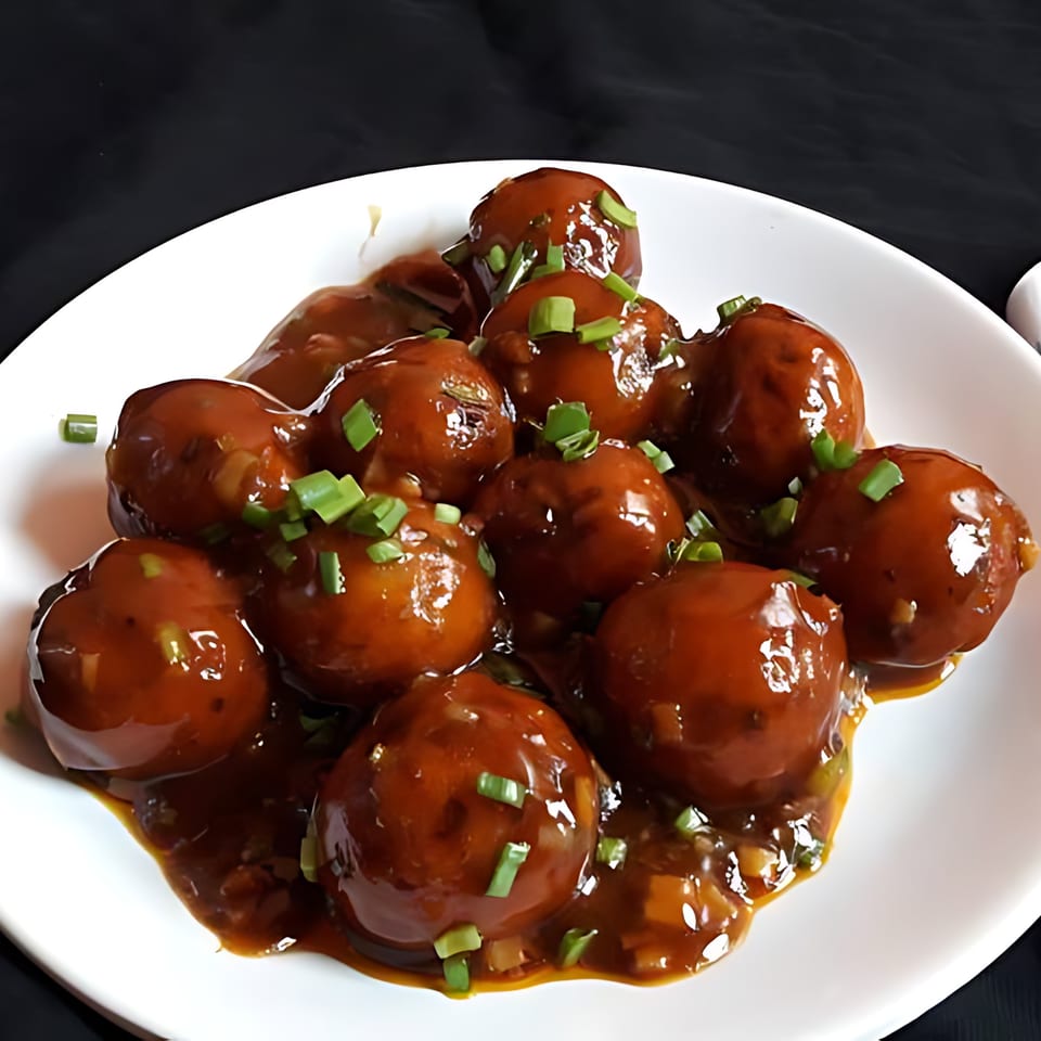 Milagu Indian Cuisine's Manchurian dish, featuring brown glazed balls garnished with chopped green onions on a white plate.