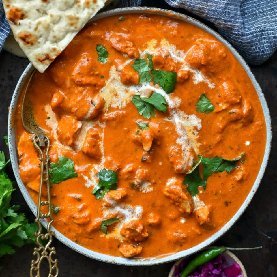 Milagu Indian Cuisine's butter chicken, garnished with cilantro and cream, served with naan.