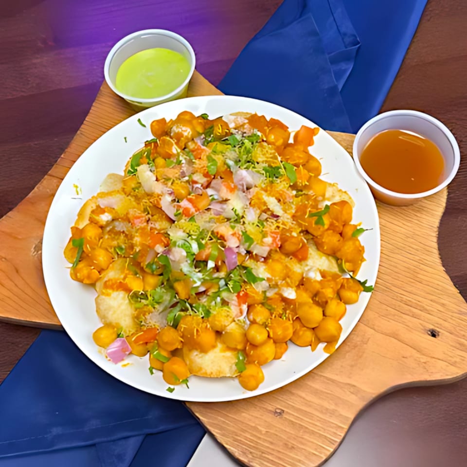 A plate of Milagu Indian Cuisine's chana chaat with chickpeas, onions, cilantro, and sauces.
