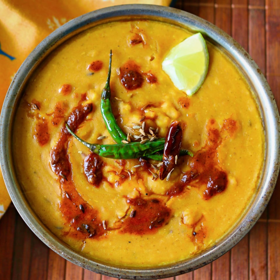 A bowl of Milagu Indian Cuisine's yellow dal, garnished with green chilies, spices, and a lime wedge.